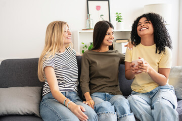 Diverse young female friends sitting on the sofa, laughing and telling stories