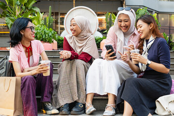 Four cheerful Asian female friends having fun enjoying drinks together in shopping mall