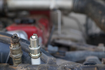 Spark plugs, old and new, for engines on the background of a car with an open hood.