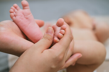 The palms of the mother are holding the foot of the newborn asian baby. Close-up family photo of a child's toes, heels and feet.