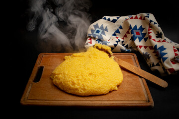 Romanian traditional mamaliga on a wooden chopping board next to a eastern motifs table cloth, on dark background
