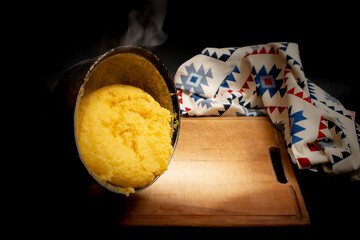 Romanian traditional mamaliga pouring on a wooden chopping board next to a eastern motifs table cloth, on dark background