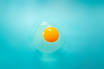 Raw cracked egg on blue background, soft focus close up, abstract texture