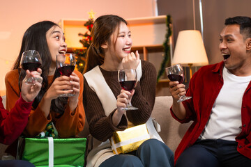 Two handsome young men and two beautiful young women wearing Christmas hats laughing joyfully at a Christmas party with delicious food, drinks and a cheerful exchange of thoughtful gifts