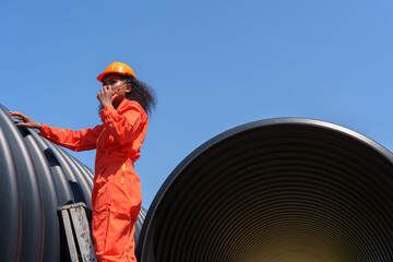 Obraz premium A black female mechanical engineer in a safety uniform inspects and inspects piping systems for a new construction project of a large industrial building.