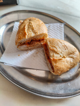 A classic M&aacute;laga "pitufo" sandwich filled with seasoned pork loin in lard, served on a silver tray. Perfect for showcasing Spanish cuisine and casual dining culture.