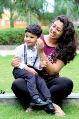 mummy is helping her 3 year old son in getting ready. Boy wearing party wear and enjoying his bond with his bother. mother and son are happy and playing in the park.  Child is ready for his school.