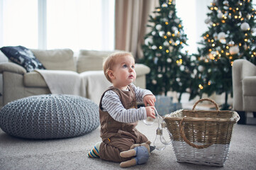 Naklejka premium Child playing with a basket of ornaments in a cozy living room decorated for the holidays