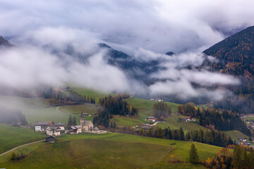 Fototapeta premium Autumn View of Santa Maddalena in the Dolomites Covered in Morning Fog with Colorful Fall Meadow and Scenic Mountain Background