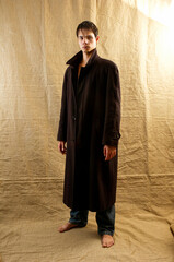 Guy standing in long black coat on beige crumpled background in studio