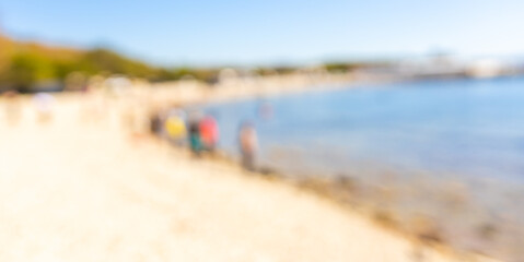 Blurred background of families enjoying a sunny day at the beach with children playing and swimming in the water during summer along the shoreline