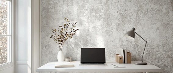 A workstation with a laptop, and desk lamp on a white table in a minimalist interior with a patterned wallpaper wall