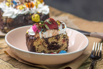   Close-up of a beautifully decorated dessert loaf cake with a rich texture, adorned with cream, fresh strawberries, and colorful chocolates. Set on a rustic table with natural elements.