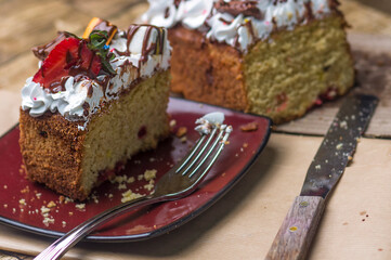   Close-up of a beautifully decorated dessert loaf cake with a rich texture, adorned with cream, fresh strawberries, and colorful chocolates. Set on a rustic table with natural elements.