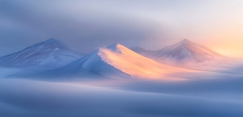 A snow-covered mountain range glowing under the light of a pale, golden sunrise ,