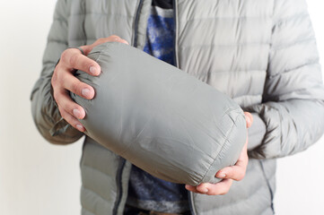 A hand holding a gray compression sack with a compact packable jacket or sleeping bag inside. Ideal for travel, camping, and hiking enthusiasts