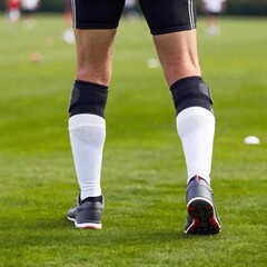 Fototapeta premium Elderly player leg, highlighting knee brace in sharp focus, with the grassy field and other players in the distance