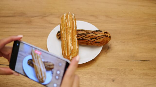Woman capturing photo of dessert on table using mobile phone. Beautifully arranged dessert highlights creativity and style. Perfect for themes of food photography dessert presentation and culinary art