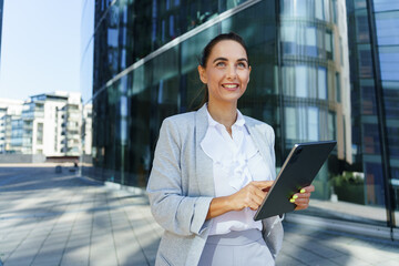 Professional Woman Using Tablet While Smiling Outside Modern Office Building During Daylight