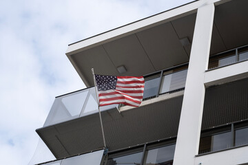A view of the American flag waving on a balcony of a modern building, symbolizing patriotism and...