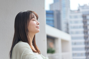 ベランダに出て深呼吸をする若い女性。