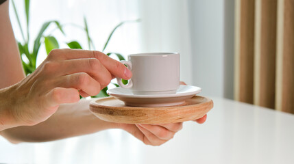 Female hand writing on blank notebook and holding coffee mug on home office desk