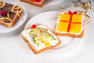 Christmas funny creative toasts sandwich for kids breakfast. Homemade Christmas morning sandwiches in form of gift, Christmas tree, deer, snowman, penguin, with cheese, fruit, chocolate, vegetables