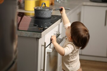 Little boy playing with pot on stove in kitchen. Dangerous situation