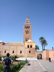 Obraz premium The Koutoubia Minaret, a Marrakech landmark, rises majestically above a lush garden, offering a striking contrast between the intricate red brickwork and the surrounding greenery against a clear blue 