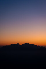 Silhouette of a mountain range at sunrise, with a stunning gradient sky transitioning from deep purple to soft orange, evoking peace and the beauty of nature’s simplicity.
