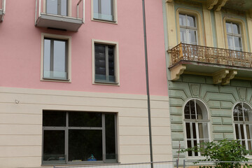 Naklejka premium The picturesque view presents a striking contrast between a modern pink apartment building and a historic green one, highlighting the diverse architectural styles within this charming neighborhood