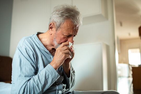 Senior man with cold blowing his nose at home