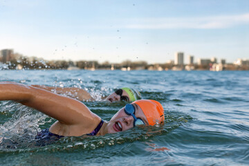 Group of athletes competing in an open water swimming race with city skyline in the background.