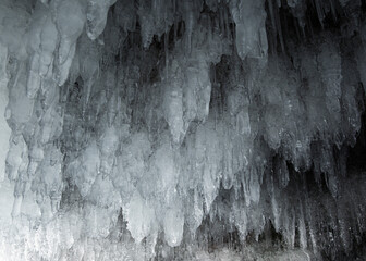 View from the ice cave on Lake Baikal. Many beautiful icicles on the walls and ceiling. Thick and thin icicles. Ice on the floor.