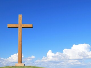 A cross standing alone against a clear blue sky with puffy white clouds in the background, outdoors, divine