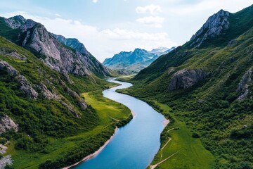 A scenic aerial view of a winding river surrounded by lush green hills and majestic mountains under a clear blue sky.