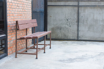 wooden bench with a metal frame placed against a brick wall. The bench has a simple design with a...