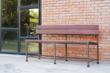 wooden bench with a metal frame placed against a brick wall. The bench has a simple design with a...