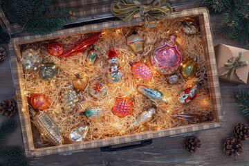 A vintage suitcase is filled with colorful holiday ornaments, surrounded by soft straw and twinkling lights, creating a cozy festive atmosphere.