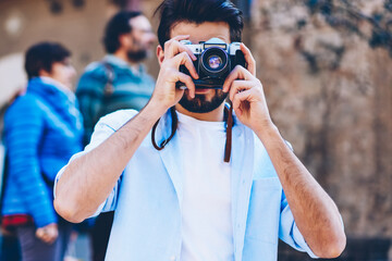 Man lover of travel focusing to take photos walking on streets of downtown during summer holiday.Tourist photographer making pictures on vintage camera with modern lenses strolling in urban setting