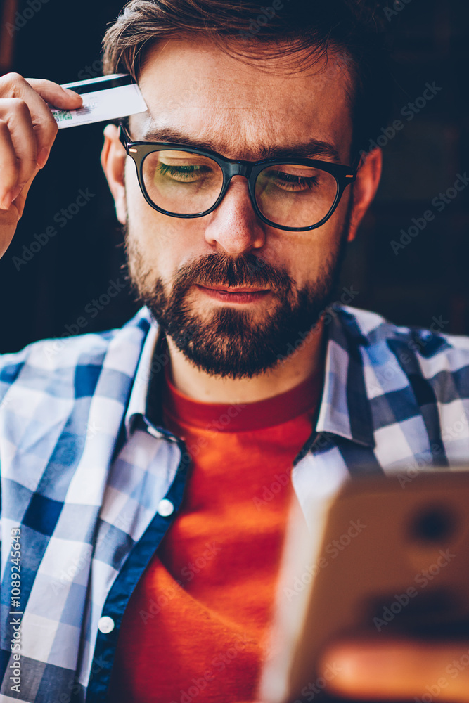 Aufkleber pensive bearded young man in optical eyeglasses for vision correction holding banking card in hands 