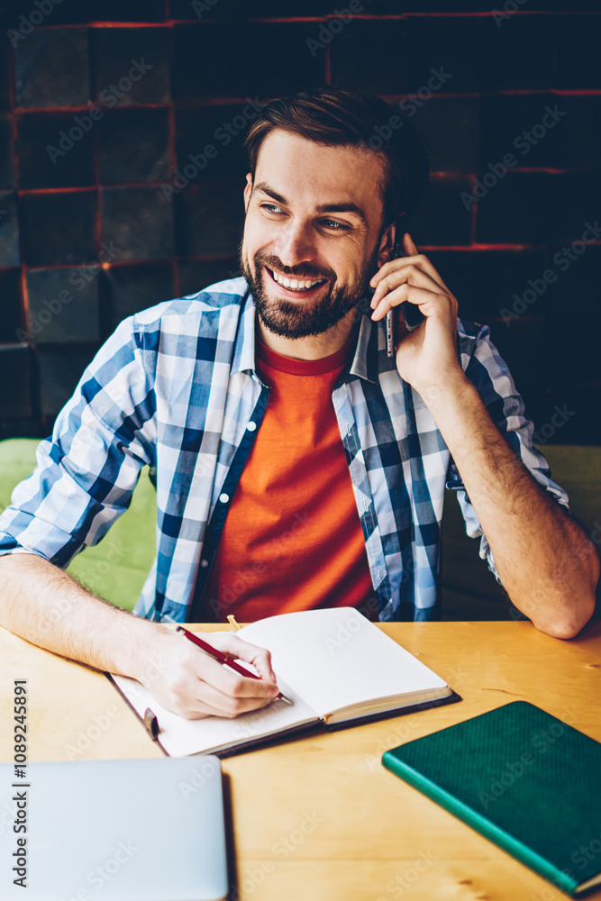 Aufkleber successful bearded student calling on smartphone device while doing homework in notepad sitting at t
