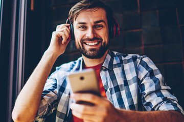 Portrait of happy bearded male blogger smiling at camera while listening songs from music...
