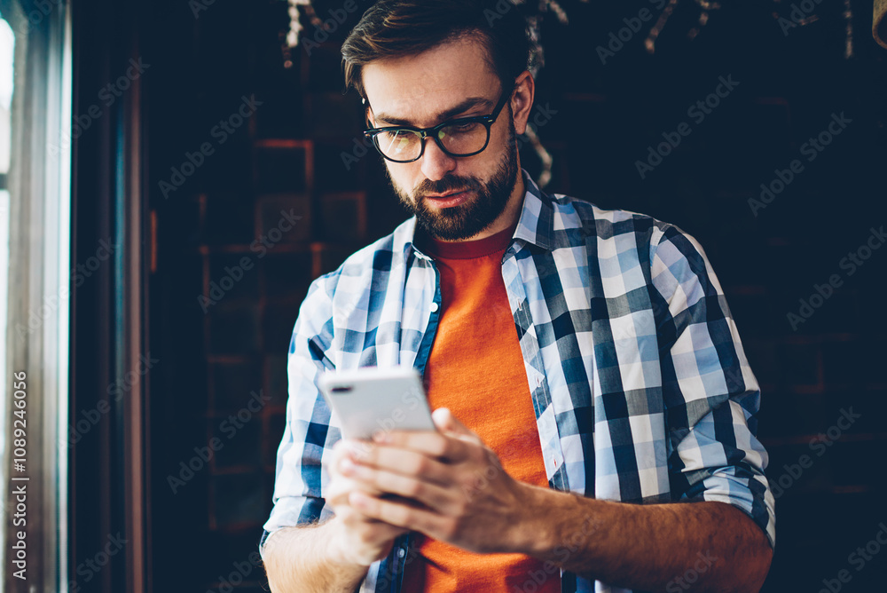 Poster pensive bearded hipster blogger reading incoming notification and chatting in networks on smartphone