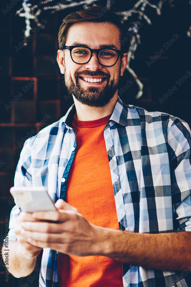 Aufkleber portrait of happy bearded young man smiling at camera while typing text message on smartphone device
