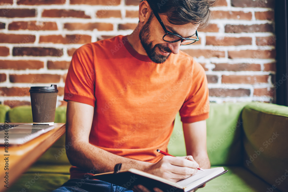 Aufkleber cheerful bearded student writing down notes of course work in notepad sitting in coworking space at 