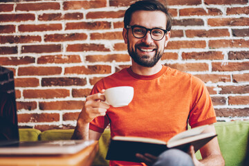 Portrait of bearded young man in eyeglasses for vision correction laughing at camera while enjoying...