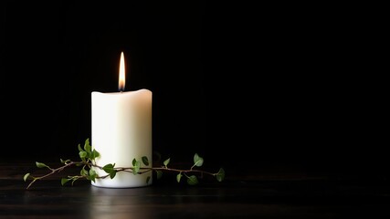 A single white burning candle with ivy wrapped around it sits on a dark wooden table against a black backdrop, somber, mourning