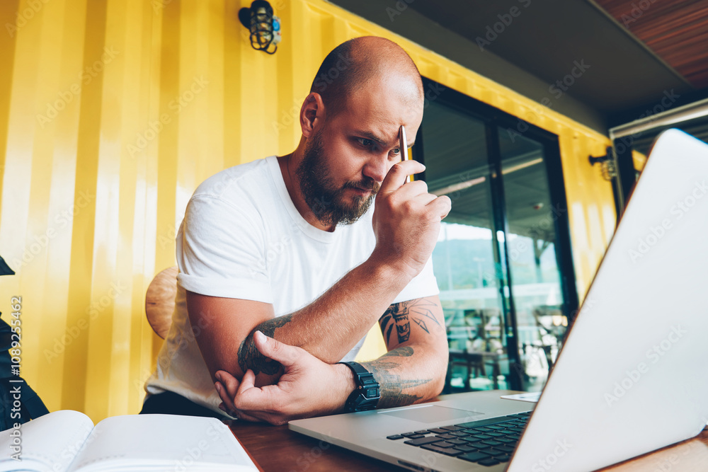 Poster concentrated male student puzzled on solving problem watching online tutorial during courses via lap