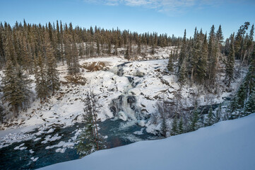 Winter overview of the frozen Cameron River and a waterfall in Hidden Lake Territorial Park, Northwest Territories, Canada